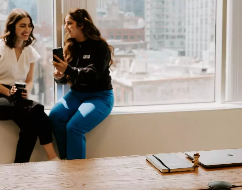 Two women sitting in a digital marketing office talking to each other.